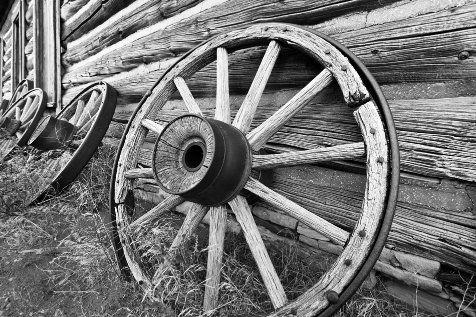 Black & White photo of old wagon wheels leaning against log building
