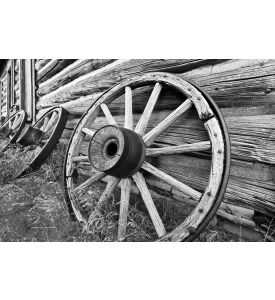 Black & White photo of old wagon wheels leaning against log building  - ID # 86092522